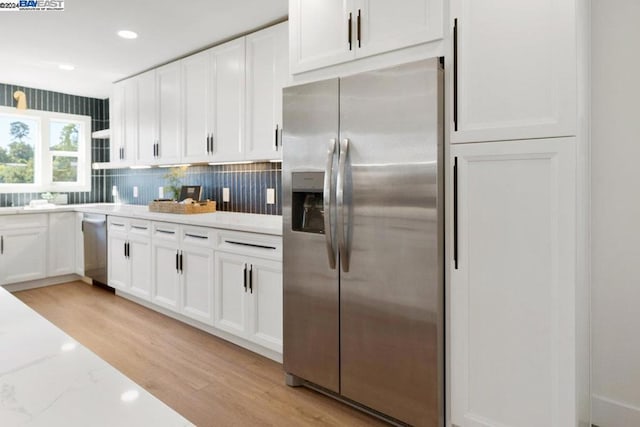 kitchen with backsplash, white cabinetry, stainless steel appliances, light stone countertops, and light hardwood / wood-style floors