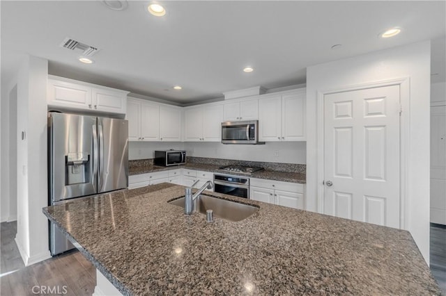 kitchen with sink, white cabinetry, a center island with sink, dark stone countertops, and stainless steel appliances