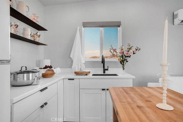 kitchen with wood counters, open shelves, white cabinets, a sink, and an AC wall unit