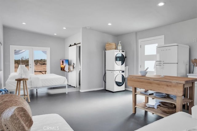 bedroom with stacked washer / dryer, white refrigerator, and a barn door