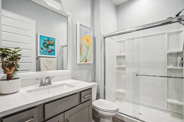 bathroom featuring a shower with door, vanity, and toilet