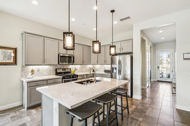 kitchen featuring light stone counters, sink, an island with sink, hanging light fixtures, and appliances with stainless steel finishes