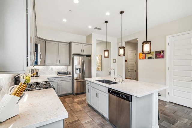 kitchen with pendant lighting, appliances with stainless steel finishes, a kitchen island with sink, and sink