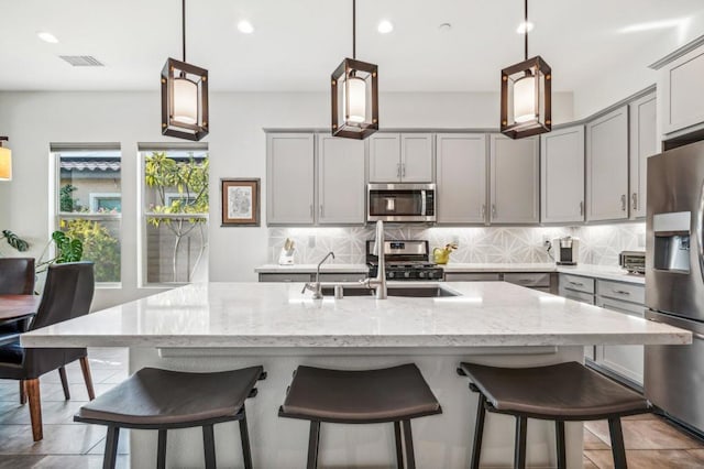 kitchen featuring appliances with stainless steel finishes, a kitchen island with sink, gray cabinets, and decorative light fixtures