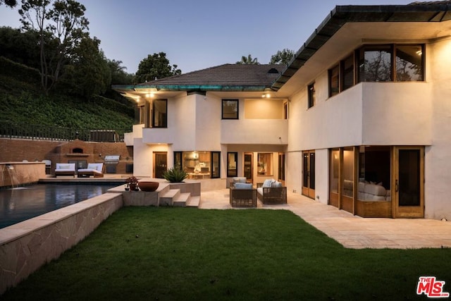 back house at dusk with an outdoor hangout area, a lawn, and a patio area