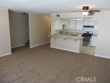 kitchen with kitchen peninsula, a kitchen breakfast bar, light colored carpet, stainless steel range oven, and white cabinets