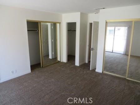 unfurnished bedroom with dark colored carpet and multiple closets