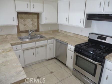 kitchen featuring sink, light tile patterned floors, appliances with stainless steel finishes, white cabinetry, and extractor fan