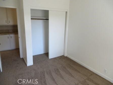 unfurnished bedroom with dark colored carpet and a closet