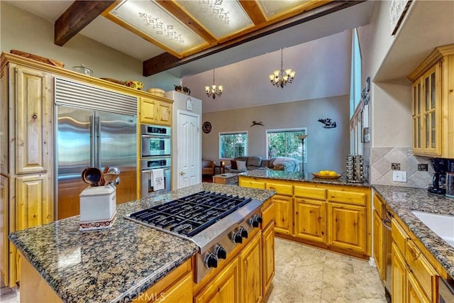 kitchen with dark stone countertops, a kitchen island, an inviting chandelier, hanging light fixtures, and appliances with stainless steel finishes