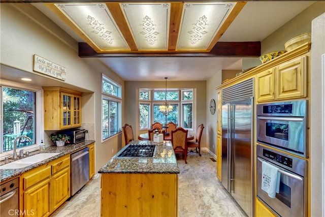 kitchen featuring dark stone countertops, a kitchen island, sink, appliances with stainless steel finishes, and a chandelier