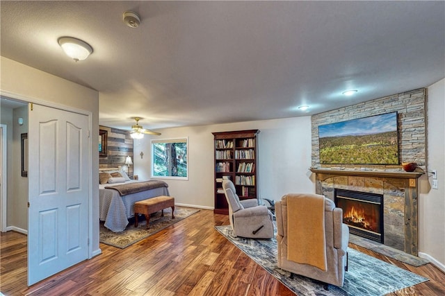 bedroom featuring ceiling fan, wood-type flooring, and a stone fireplace