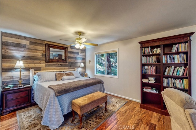 bedroom featuring ceiling fan, light hardwood / wood-style flooring, and wood walls