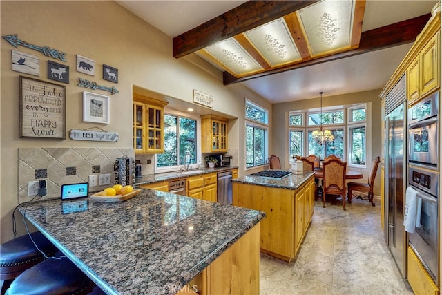 kitchen featuring stainless steel appliances, dark stone counters, a chandelier, pendant lighting, and a center island