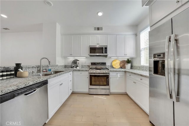 kitchen with white cabinets, stainless steel appliances, light stone countertops, and sink