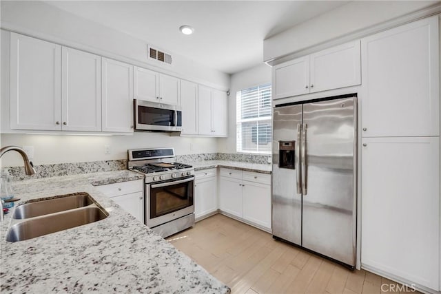 kitchen featuring light stone counters, stainless steel appliances, white cabinetry, and sink