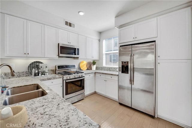 kitchen with light stone counters, stainless steel appliances, white cabinetry, and sink