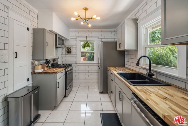 kitchen featuring stainless steel appliances, sink, a chandelier, gray cabinets, and butcher block counters