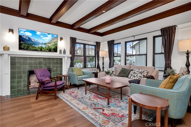 living room with a tiled fireplace, beam ceiling, and light wood-type flooring