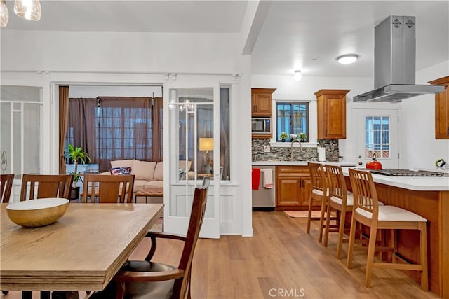 kitchen featuring tasteful backsplash, appliances with stainless steel finishes, island range hood, light hardwood / wood-style floors, and decorative light fixtures