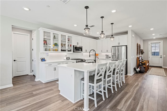 kitchen with light wood-type flooring, sink, white cabinetry, a center island with sink, and appliances with stainless steel finishes