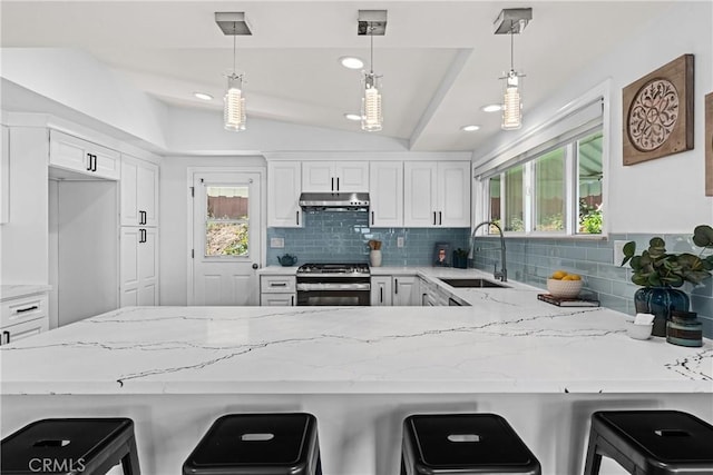 kitchen with kitchen peninsula, vaulted ceiling, sink, stainless steel gas range, and a breakfast bar area