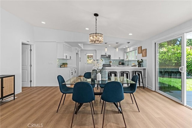 dining area with sink, light wood-type flooring, a chandelier, and vaulted ceiling