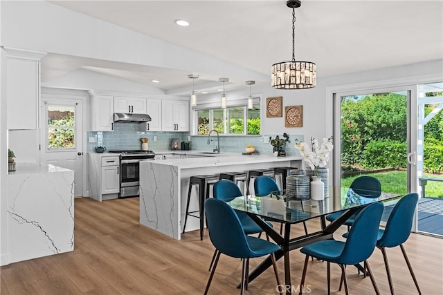 kitchen with vaulted ceiling, hanging light fixtures, stainless steel stove, white cabinets, and tasteful backsplash