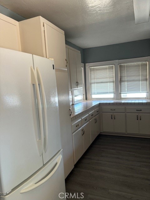 kitchen with white refrigerator, tile counters, a textured ceiling, dark wood-type flooring, and white cabinets