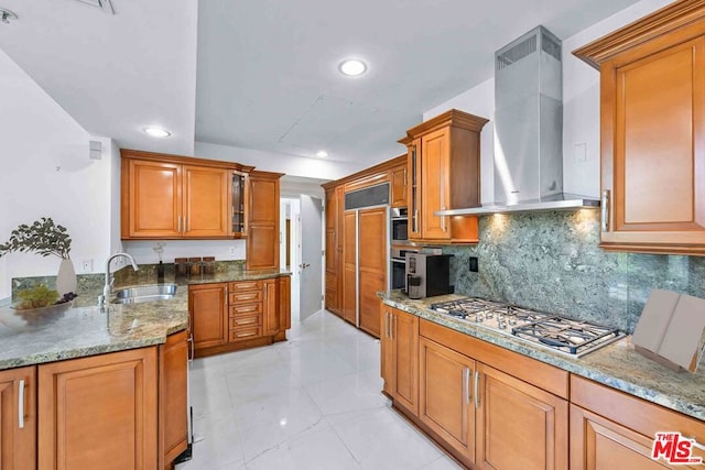 kitchen with wall chimney range hood, sink, light tile patterned floors, appliances with stainless steel finishes, and light stone counters