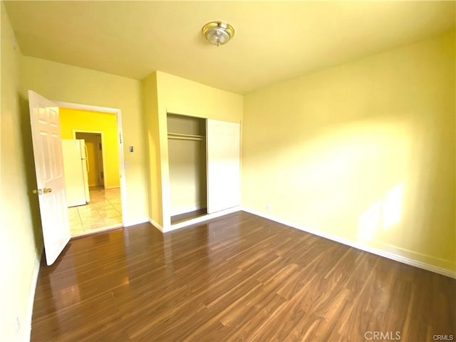 unfurnished bedroom featuring white fridge, wood-type flooring, and a closet