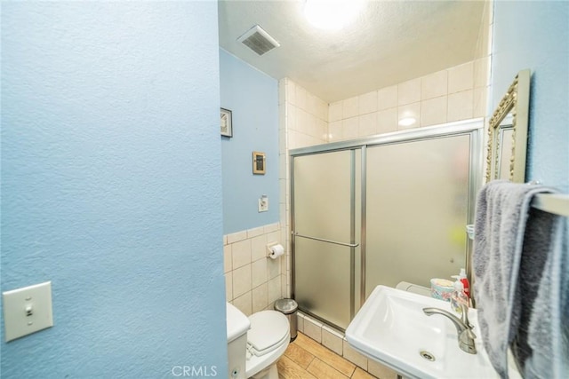 bathroom featuring sink, a shower with door, tile walls, and toilet