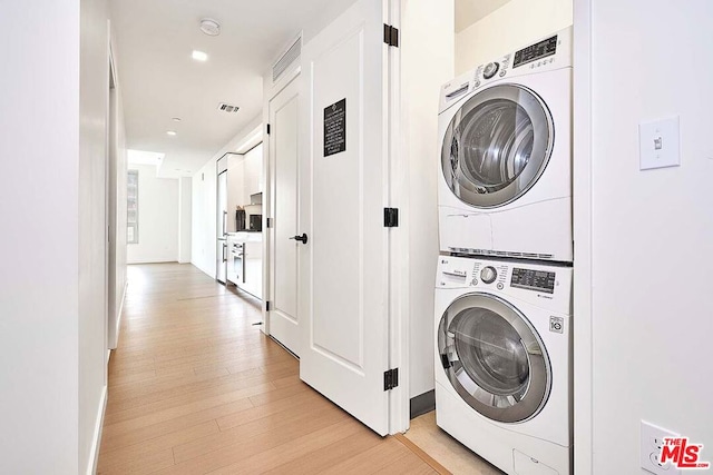 clothes washing area featuring light hardwood / wood-style flooring and stacked washer and clothes dryer