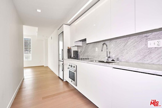 kitchen with sink, white cabinets, light hardwood / wood-style flooring, and oven