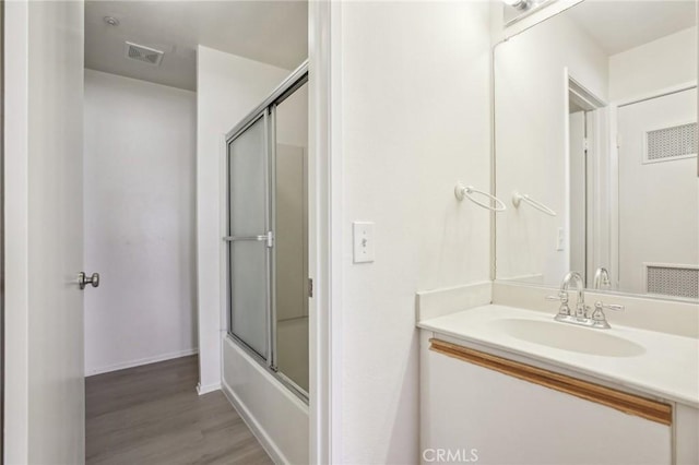 bathroom with wood-type flooring, shower / bath combination with glass door, and vanity