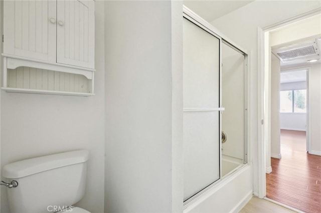 bathroom with wood-type flooring, enclosed tub / shower combo, and toilet