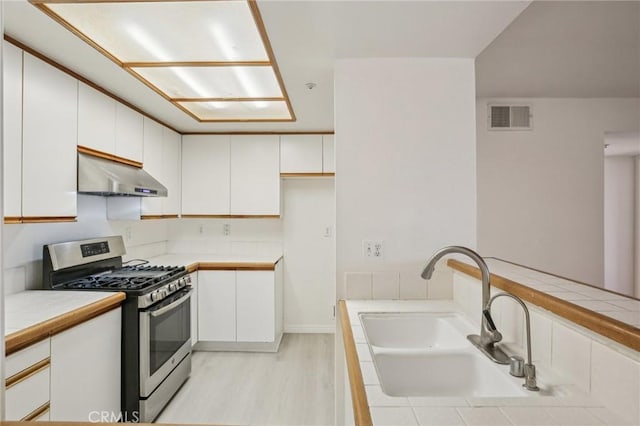 kitchen featuring gas stove, sink, tile countertops, and white cabinets