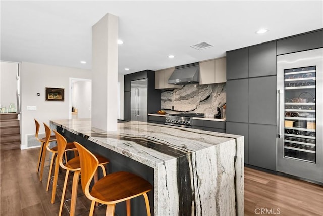 kitchen with a kitchen bar, light stone countertops, gray cabinetry, extractor fan, and hardwood / wood-style flooring