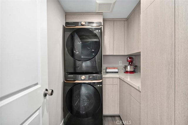 laundry room featuring cabinets, wood-type flooring, and stacked washer / dryer