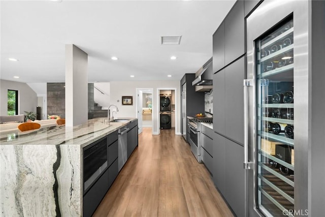 kitchen with sink, light stone counters, ventilation hood, light hardwood / wood-style floors, and high quality appliances