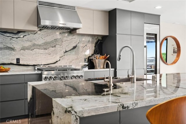 kitchen featuring exhaust hood, hardwood / wood-style flooring, gray cabinets, light stone countertops, and tasteful backsplash