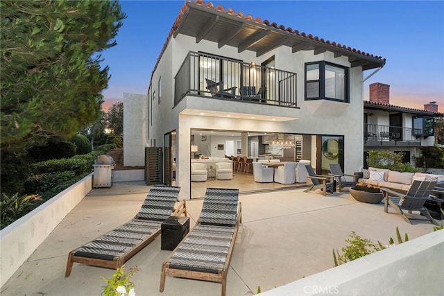 back house at dusk with a patio area, an outdoor living space, and a balcony