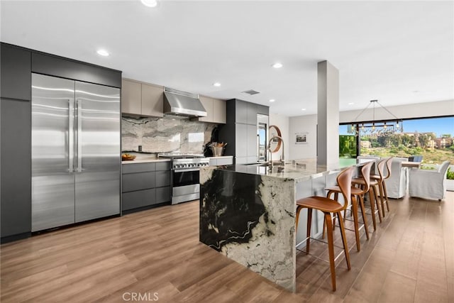 kitchen featuring light wood-type flooring, gray cabinetry, a breakfast bar, high end appliances, and exhaust hood