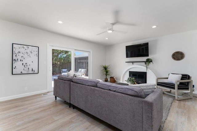 living room with a fireplace, ceiling fan, and light wood-type flooring