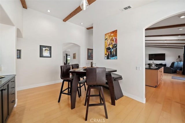 dining space featuring light wood-style floors, visible vents, arched walkways, and beam ceiling