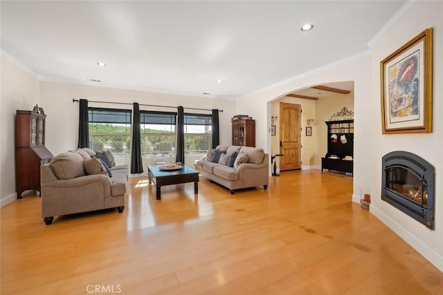 living room with arched walkways, baseboards, light wood finished floors, a glass covered fireplace, and crown molding