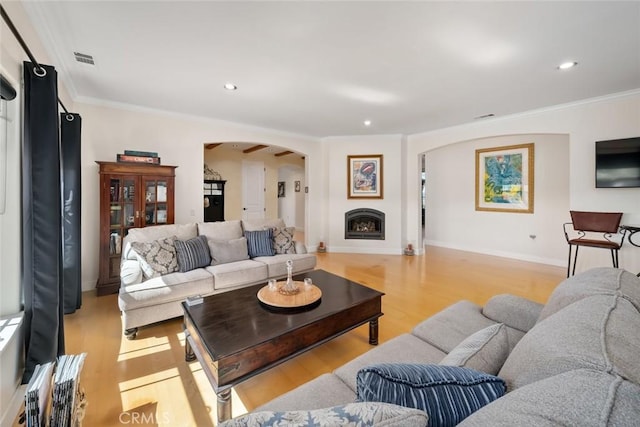 living area with ornamental molding, arched walkways, a fireplace, and light wood finished floors