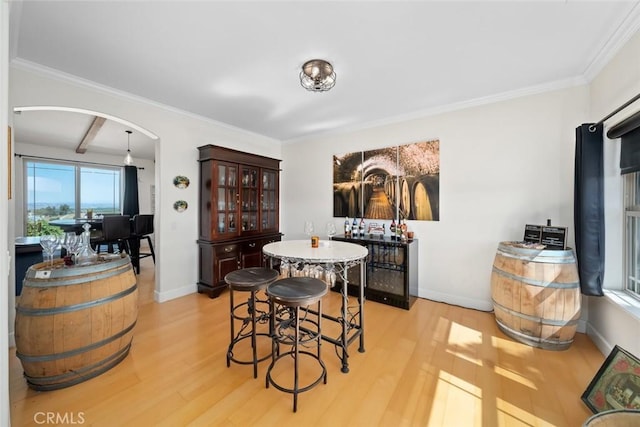 dining space featuring light wood-style floors, baseboards, arched walkways, and ornamental molding