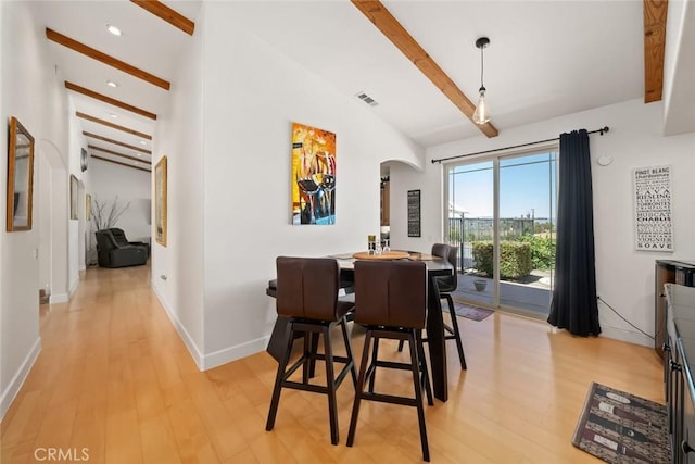 dining area with visible vents, arched walkways, baseboards, light wood-style flooring, and vaulted ceiling with beams