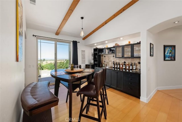 dining space with arched walkways, baseboards, bar, vaulted ceiling with beams, and light wood-style floors